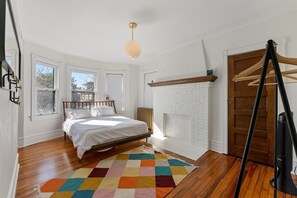 Une chambre à coucher avec un lit, un tapis coloré, une cheminée en briques blanches et une porte en bois.
