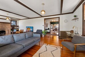 A spacious living room with a fireplace, a grey sofa, a coffee table, and a wooden floor. - Spacious 7BR Beach House with Arcade and Porch! (Wildwood)