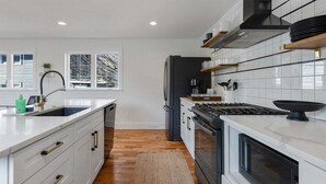 Een moderne keuken met witte kastjes, een centraal eiland, een fornuis en een koelkast.