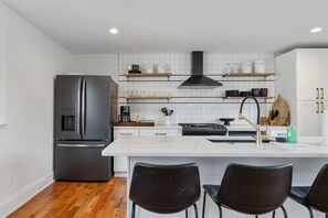 Une cuisine moderne dotée d’un îlot central, d’appareils électroménagers en acier inoxydable et d’étagères en bois.