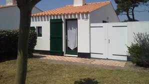 Un petit bâtiment d’un seul étage, avec un toit recouvert de tuiles, une porte verte et une clôture blanche.