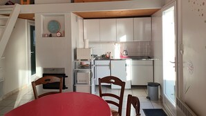 Une cuisine avec des meubles blancs, une table à manger avec des chaises, une horloge et un ventilateur de plafond.