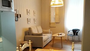 A dining area with a wooden table set for four, a sofa, a small round table, and a chair. - Apartamento Centro Córdoba Alfa (Córdoba)