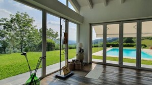 A spacious room with large sliding glass doors leading to a pool area, a green lawn, and a view of the surrounding landscape.