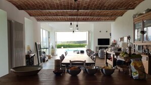 A spacious dining area with a long table, multiple chairs, and a view of a swimming pool and greenery outside.