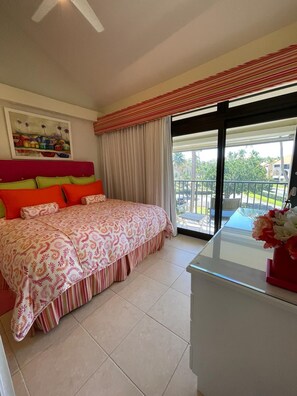 A bedroom with a bed, a painting on the wall, and a balcony with a railing.