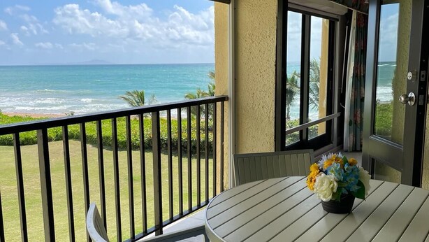 A balcony with a view of the ocean, a round table with a flower vase, and a bench. - Breathtaking Oceanfront Villa Close to Beach(183) (Humacao)