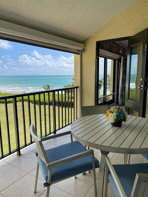 A balcony with a table and chairs, overlooking a beach and ocean.