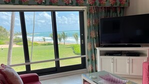 A living room with a large window, a flat-screen TV, a pink sofa, and a glass coffee table. - Breathtaking Oceanfront Villa Close to Beach(183) (Humacao)