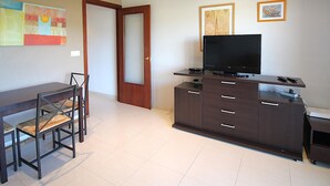 Una sala moderna con un televisor de pantalla plana sobre un mueble de madera, una mesa de comedor con sillas y dos cuadros en la pared.