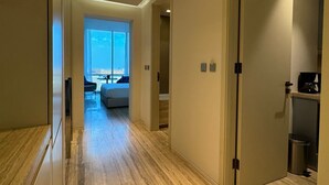 Ein moderner Flur mit Holzboden, einer Tür zu einem Zimmer mit Ausblick und einem zur Rechten liegenden Küchenbereich.