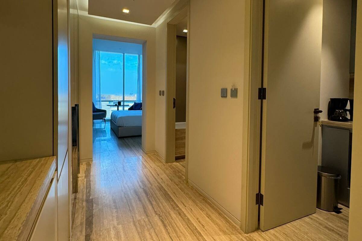 Ein moderner Flur mit Holzboden, einer Tür zu einem Zimmer mit Ausblick und einem zur Rechten liegenden Küchenbereich.