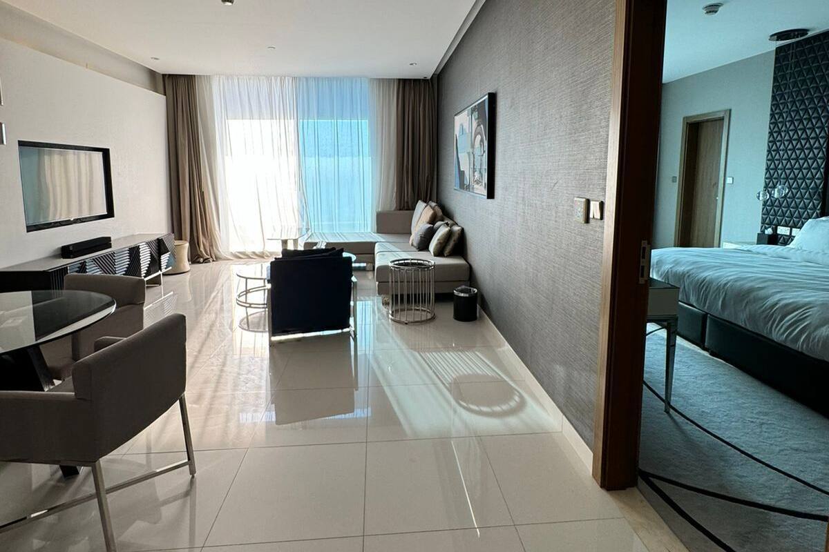 Ein modernes Hotelzimmer mit einem Glastisch, einer Couch, einem Bett und einem großen Fenster mit Vorhängen.