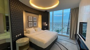 Ein modernes Hotelzimmer mit einem großen Bett, einem Nachttisch, einem Fernseher und einem großen Fenster mit Blick auf die Stadt.