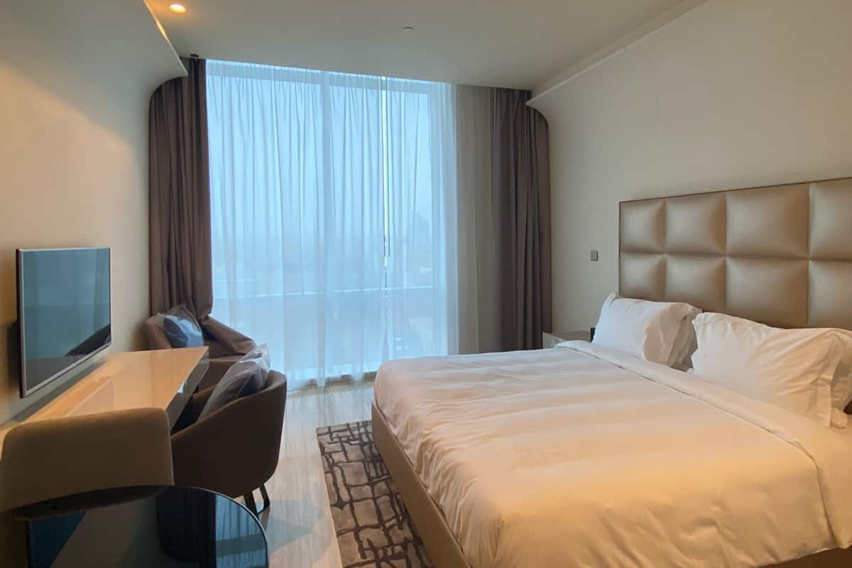 Ein modernes Hotelzimmer mit einem großen Bett, einem Schreibtisch mit Stuhl, einem Flachbildfernseher und einem großen Fenster mit Vorhängen.