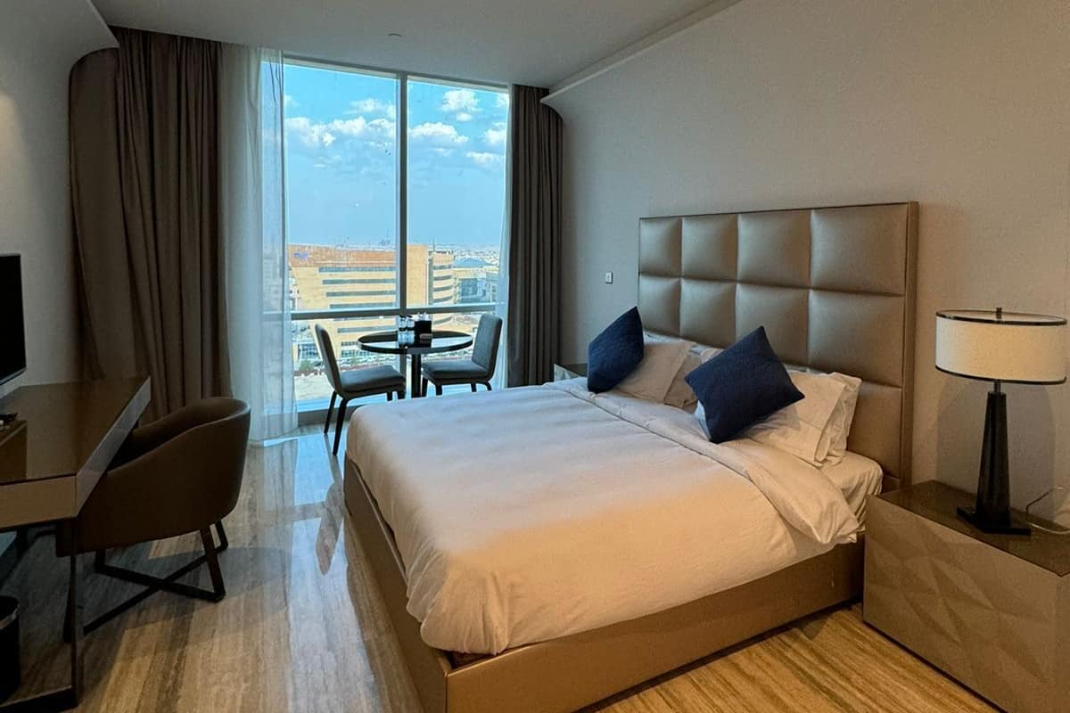 Ein Hotelzimmer mit einem großen Bett, einem Schreibtisch, einem Stuhl, einem Tisch und Blick auf die Stadt.
