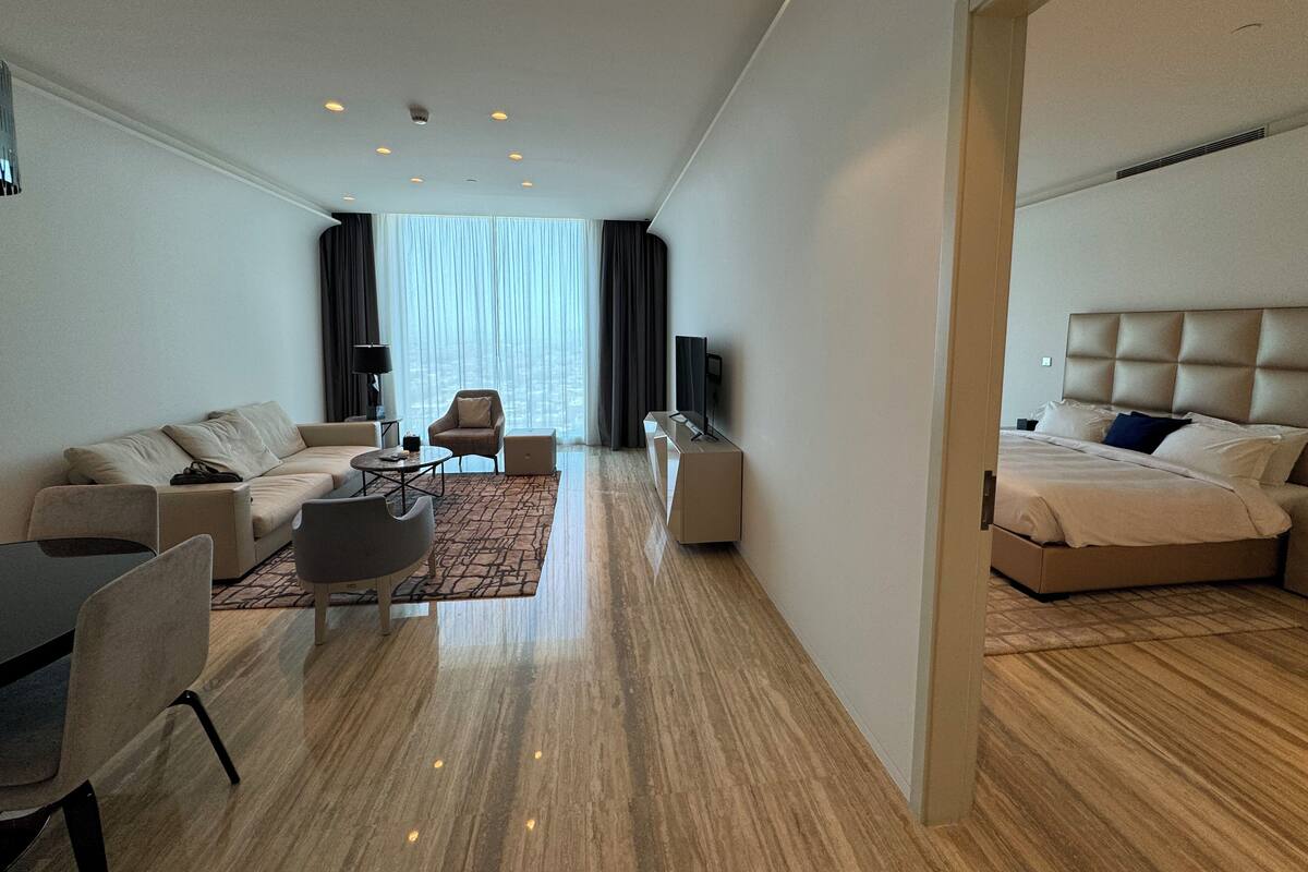 Ein modernes Hotelzimmer mit Sofa, Sessel, Esstisch und einem Bett mit Kopfteil.