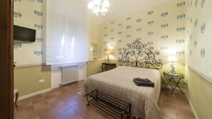 A bedroom with a bed, a radiator, a TV mounted on the wall, a chandelier, and patterned wallpaper. - Family room with 2 double or twin rooms near the port and the Venice district. (Livorno)
