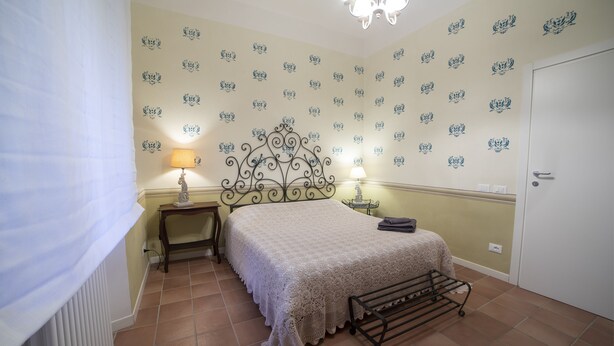 A bedroom with a bed, a nightstand, a lamp, a radiator, and a door. - Family room with 2 double or twin rooms near the port and the Venice district. (Livorno)