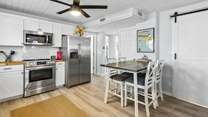A modern kitchen with white cabinetry, stainless steel appliances, and a dining area with a wooden table and chairs. - Stay Longer, Save More (Fernandina Beach)