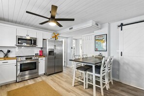 A modern kitchen with white cabinetry, stainless steel appliances, and a dining area with a wooden table and chairs.