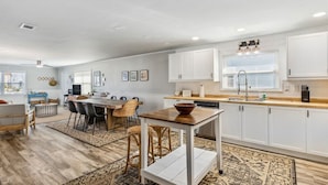 A modern kitchen with white cabinets, a wooden dining table, and a large rug. - Perfect for Projects, Travels, or Transitions (Fernandina Beach)