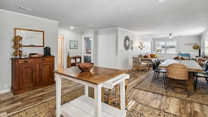 A spacious living area with a wooden dining table, a white bench, and a kitchen area with a wooden cabinet and a whiteboard. - Perfect for Projects, Travels, or Transitions (Fernandina Beach)