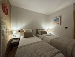 A hotel room with two beds, a wooden accent wall, a small table with a lamp, and a framed picture on the wall.