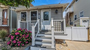A two-story house with a front porch, a mailbox, and a small garden with pink flowers. - Professionally Managed | 3 Blocks to Beach (Seaside Heights)