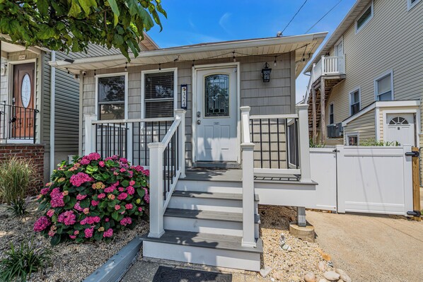 A two-story house with a front porch, a mailbox, and a small garden with pink flowers. - Professionally Managed | 3 Blocks to Beach (Seaside Heights)