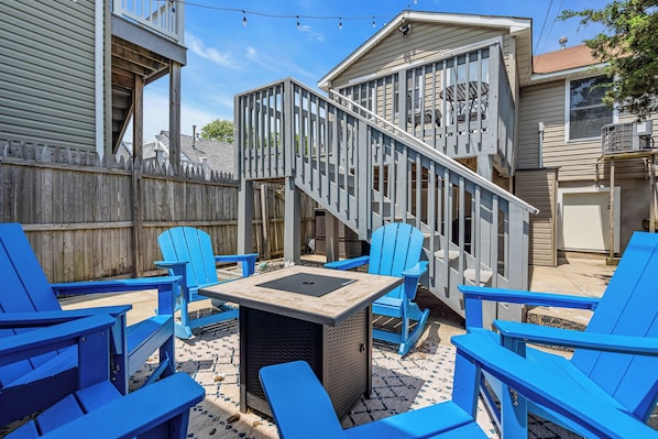 A backyard with blue Adirondack chairs, a small table, and a wooden deck with a staircase.