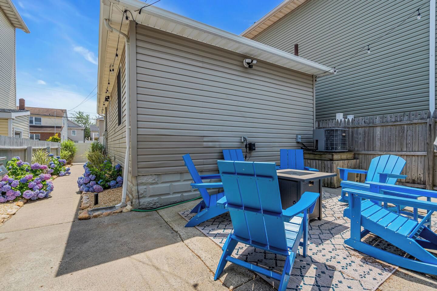 Eine Terrasse mit blauen Adirondack-Stühlen, einem kleinen Tisch und einem Grill.