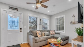A living room with a grey sofa, a ceiling fan, and a television on the wall. - Professionally Managed | 3 Blocks to Beach (Seaside Heights)