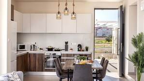 Una cocina moderna con armarios de madera, un comedor con mesa y sillas, y vistas a través de una puerta abierta.