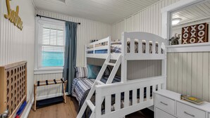 Un lit superposé avec un bureau et des tiroirs, une fenêtre avec des stores et une décoration murale en bois.
