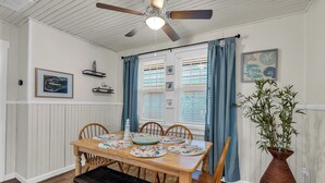 Un coin repas avec une table en bois, des chaises, un banc, un ventilateur de plafond et une plante en pot.