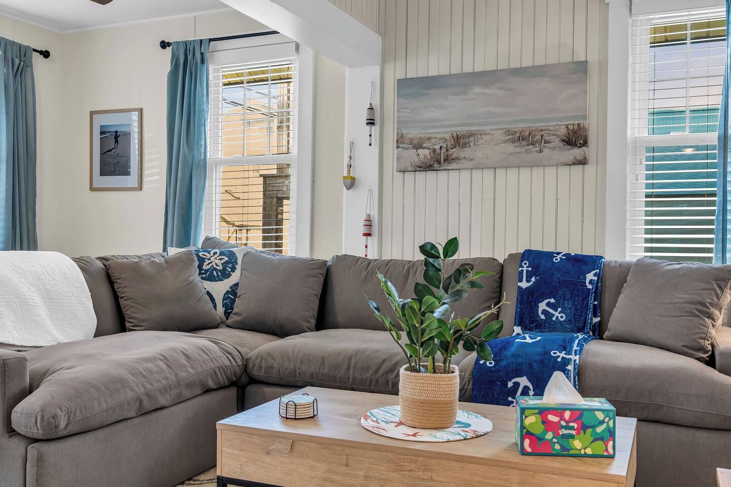 A living room with a sectional sofa, a coffee table, a potted plant, and a painting on the wall.