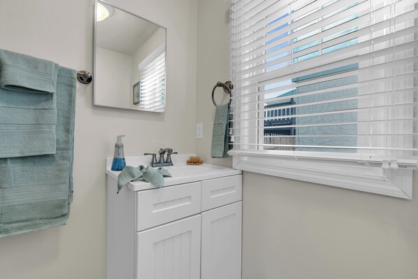A bathroom with a white sink, a mirror, and a window with blinds.