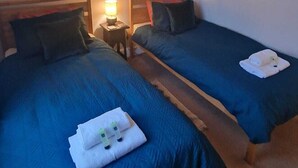 Una habitación de hotel con dos camas, cada una con cabecero de madera, una mesita de noche con lámpara y una toalla en el suelo.