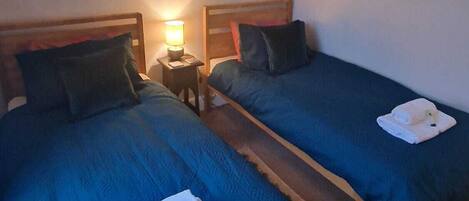 A hotel room with two beds, each with a wooden headboard, a nightstand with a lamp, and a towel on the floor.