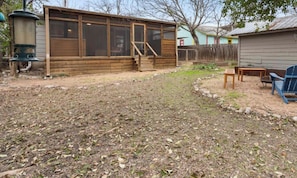A wooden structure with a screened porch, a small table, and a blue chair in the yard.