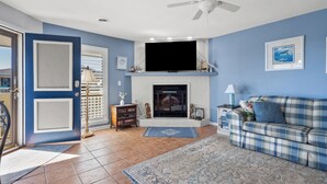 A living room with a fireplace, a television mounted above it, and a plaid sofa. - Tilghman Lakes By the Sea (North Myrtle Beach)