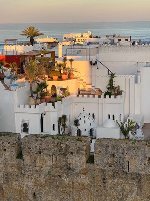 A coastal town with white buildings, a view of the sea, and a fortified wall in the foreground.