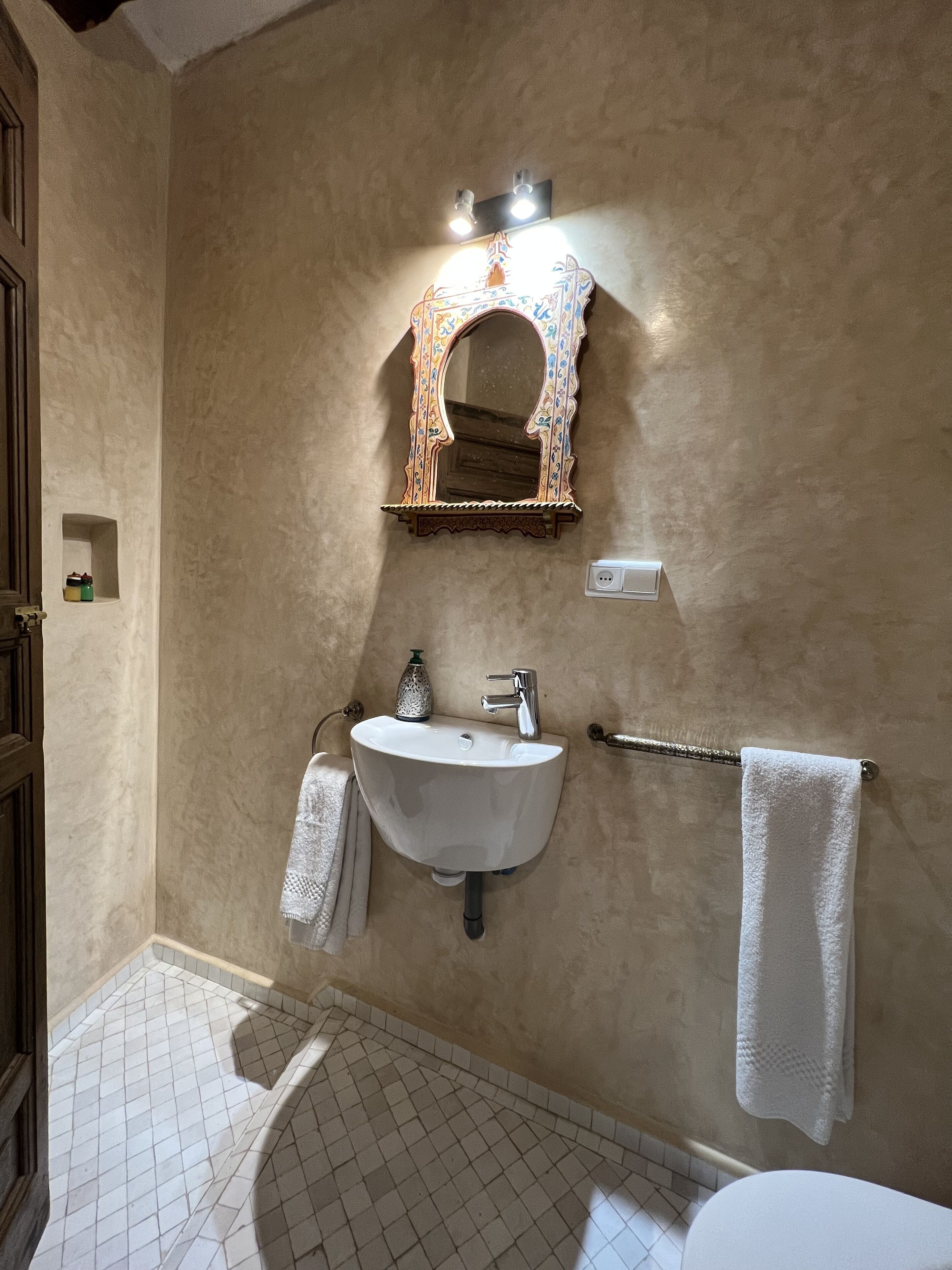 Een badkamer met een wit wastafel, een spiegel met een sierlijk frame, een handdoekrek en een douchegedeelte.
