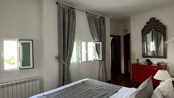 Un dormitorio con cama, cómoda, espejo y ventana con cortinas.