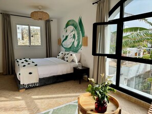 A bedroom with a bed, a nightstand, a window, and a view of the outside.