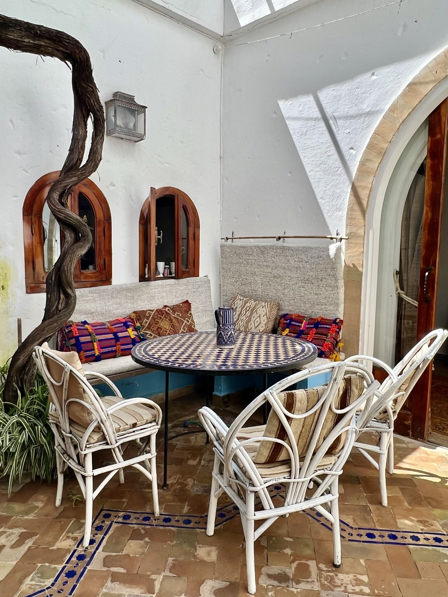 Une terrasse accueillante avec une table ronde, des chaises en osier et des coussins colorés.