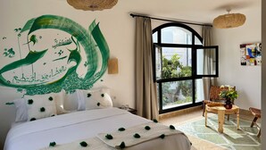 Una habitación de hotel con una cama grande, un ventanal con vistas a la vegetación, una lámpara de techo tejida y una mesita con una planta.