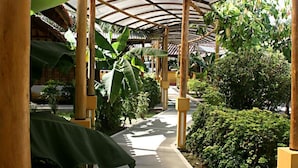 A covered walkway with a curved roof, surrounded by lush greenery and plants.