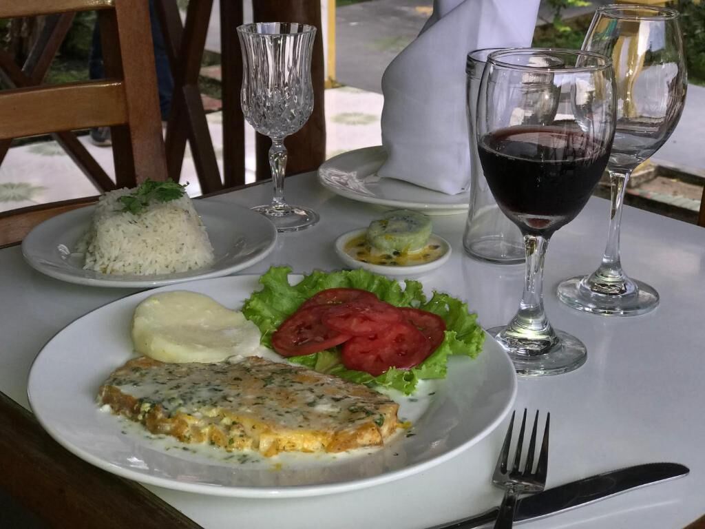 A dining table with a plate of food, including a fish fillet, rice, and vegetables, and two glasses of red wine.